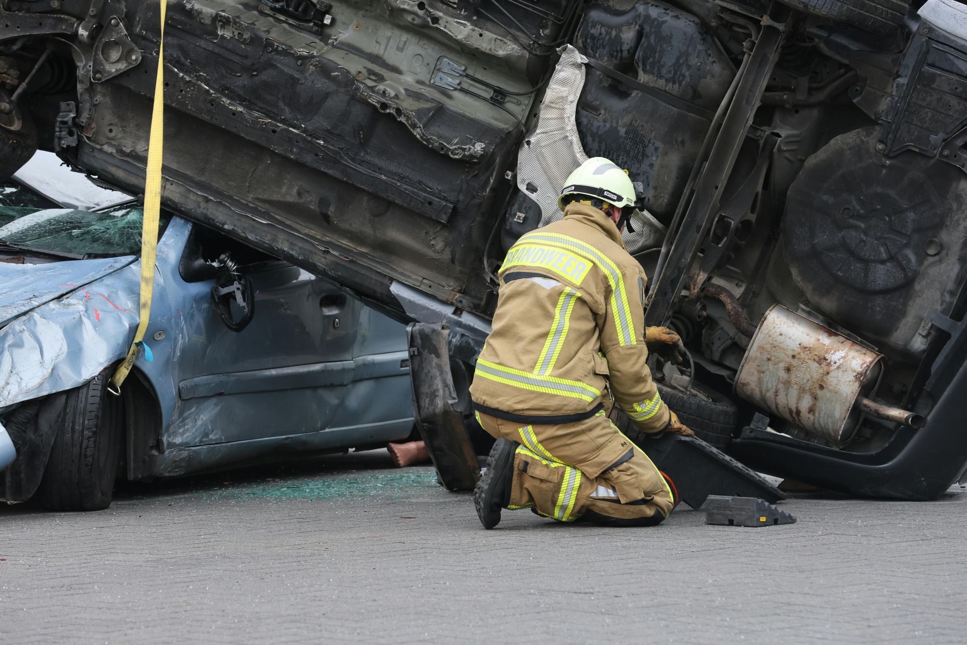 Firefighter kneeling beside a crushed car under a flipped vehicle after a crash