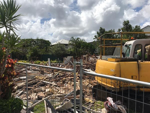 A yellow excavator is sitting on top of a pile of rubble behind a fence.