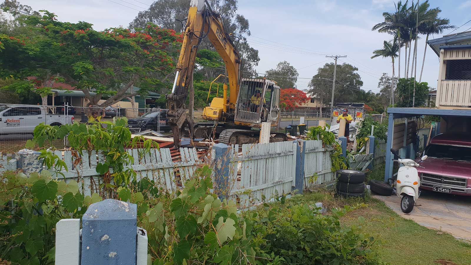A bulldozer is demolishing a fence in front of a house.