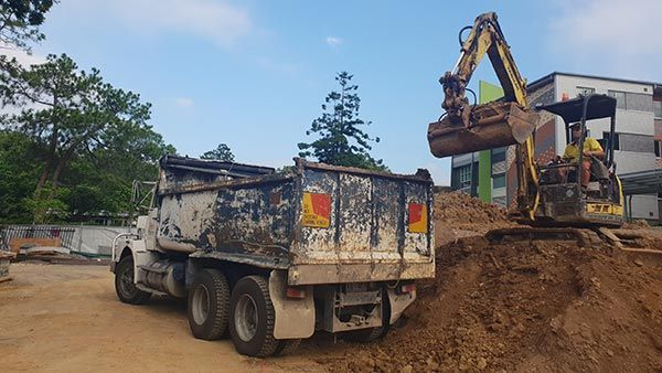 A dump truck is being loaded with dirt by an excavator.