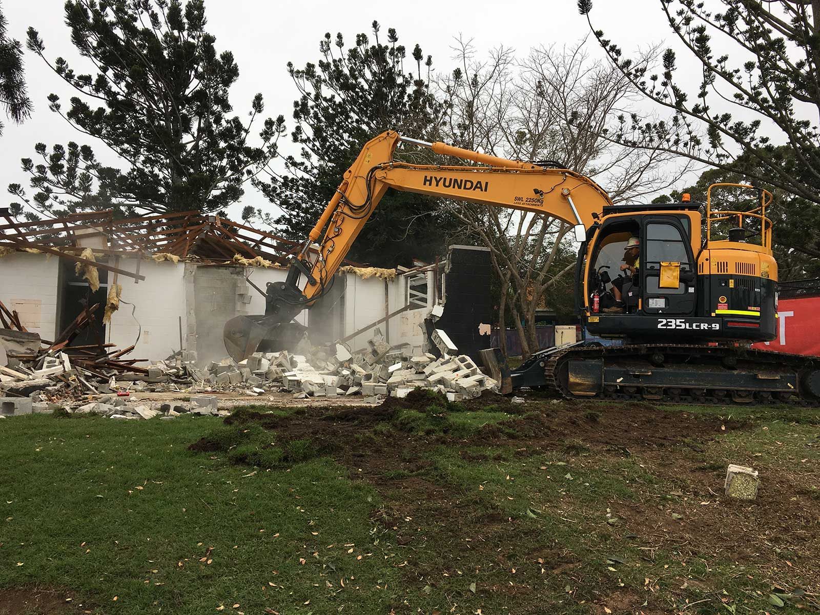 A large yellow excavator is demolishing a house.