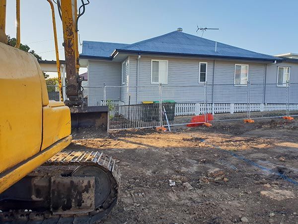 A yellow excavator is digging a hole in front of a house.