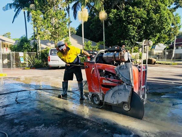 A man is cutting concrete with a machine in a parking lot.