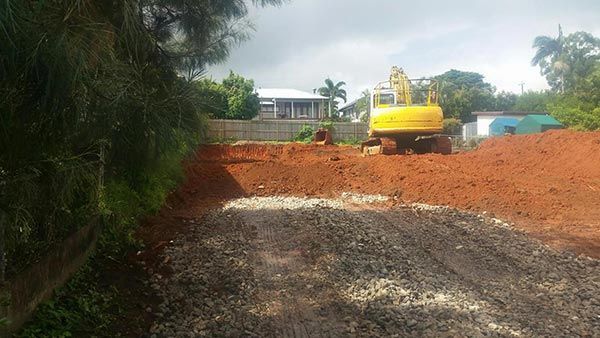A yellow excavator is driving down a dirt road.