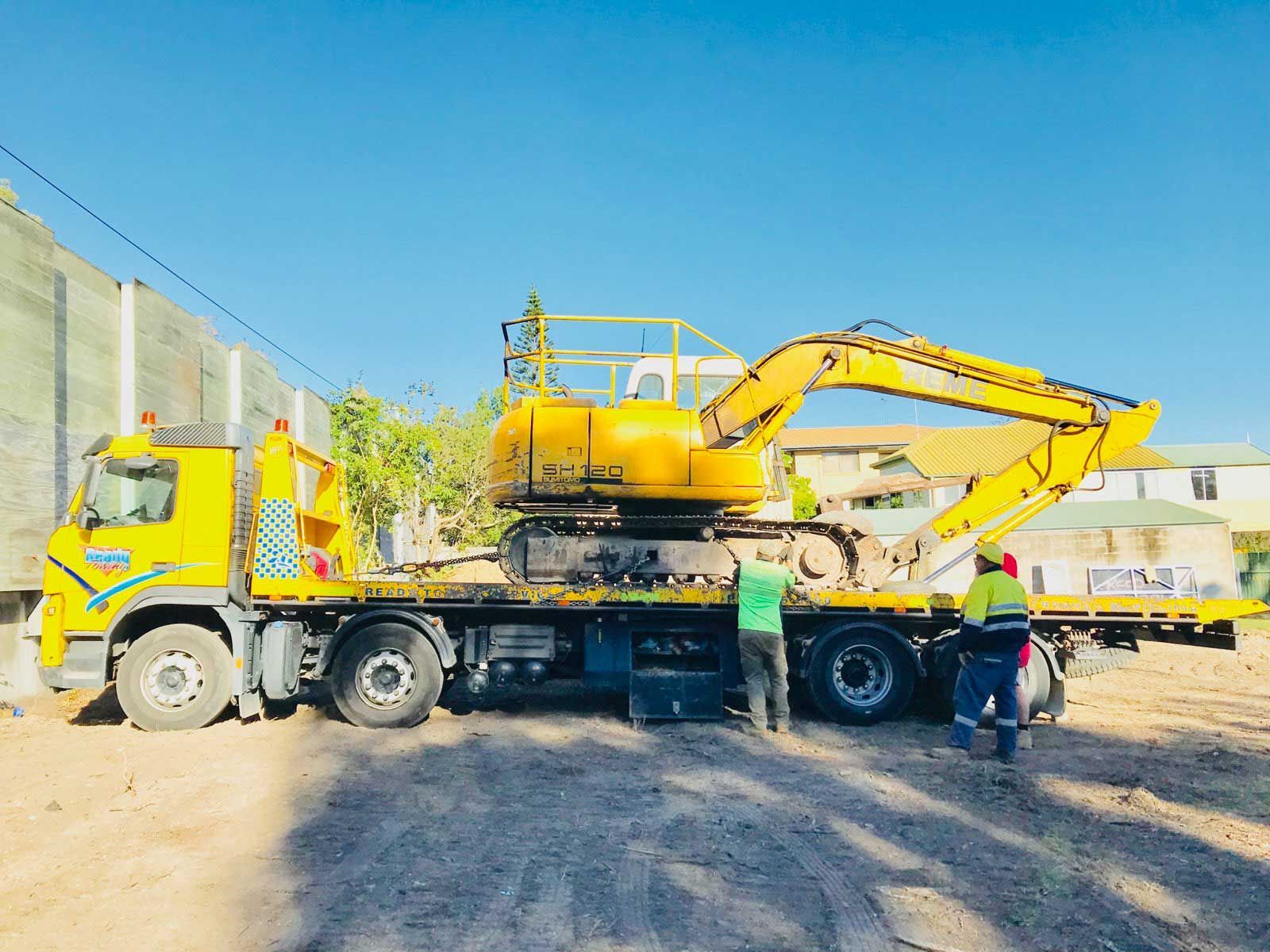 A yellow truck is towing a yellow excavator on a flatbed trailer.
