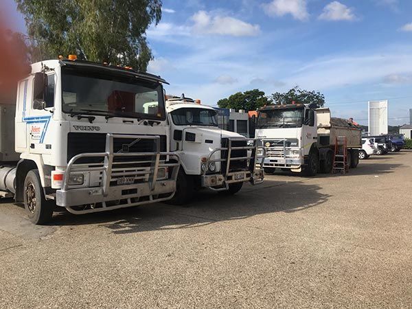 A row of trucks are parked in a gravel lot.