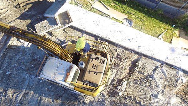 An aerial view of a construction site with a yellow excavator carrying boxes.