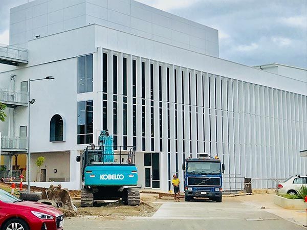 A blue kobelco excavator is parked in front of a large white building.