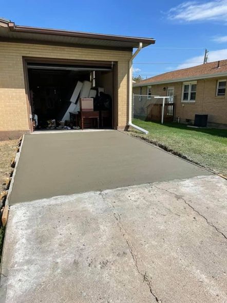 Freshly poured concrete driveway leading to a garage; old, cracked concrete in foreground.