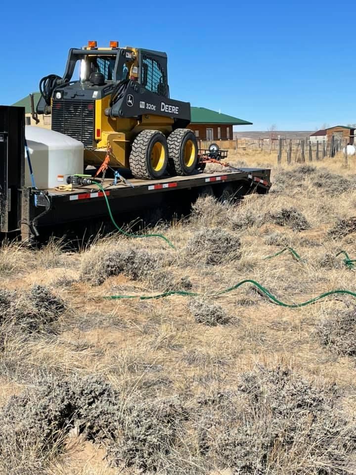 Yellow skid steer with tank on a trailer spraying brush in a field.