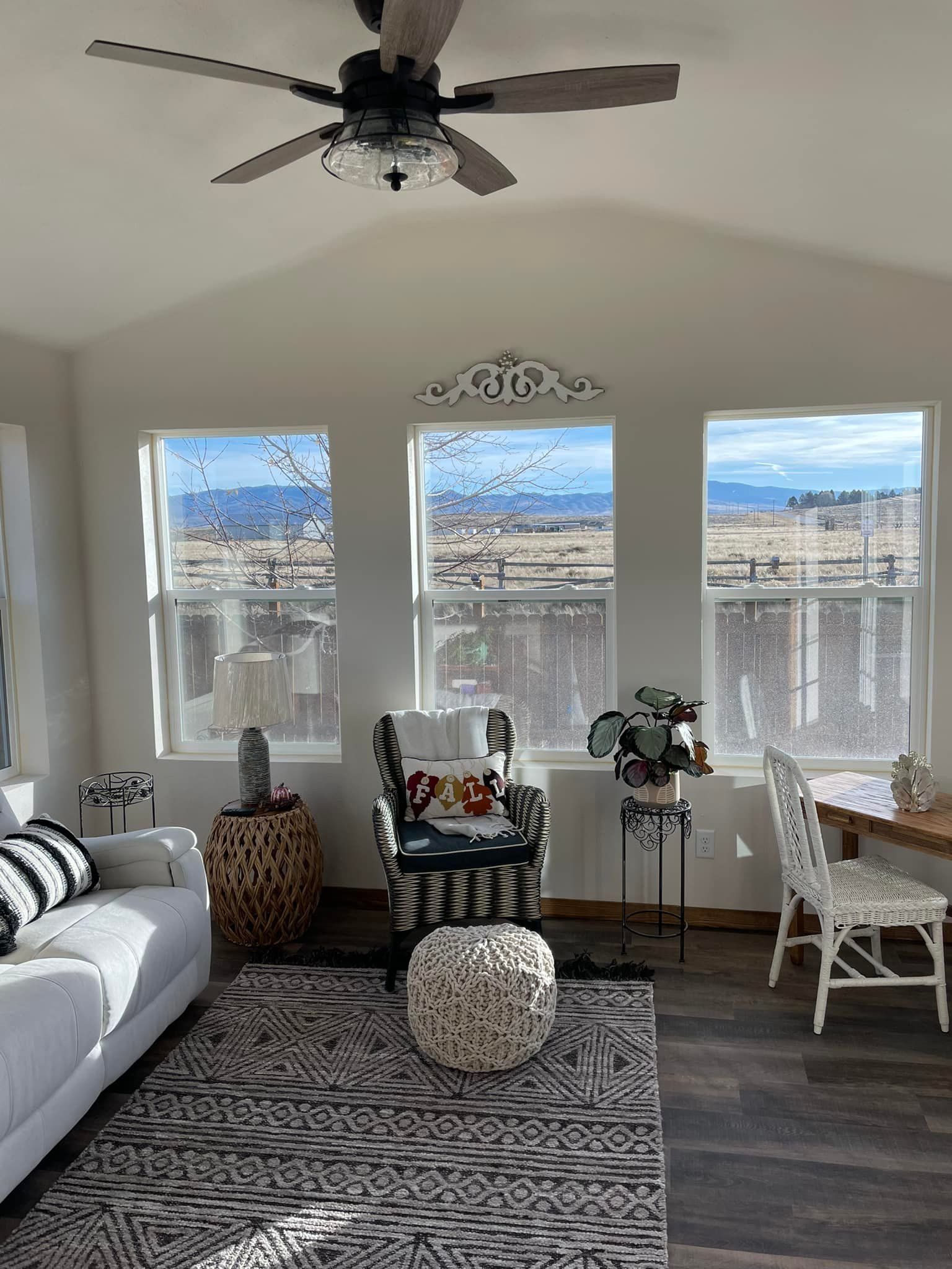 Living room with three windows overlooking a rural landscape, white walls, and a patterned rug.