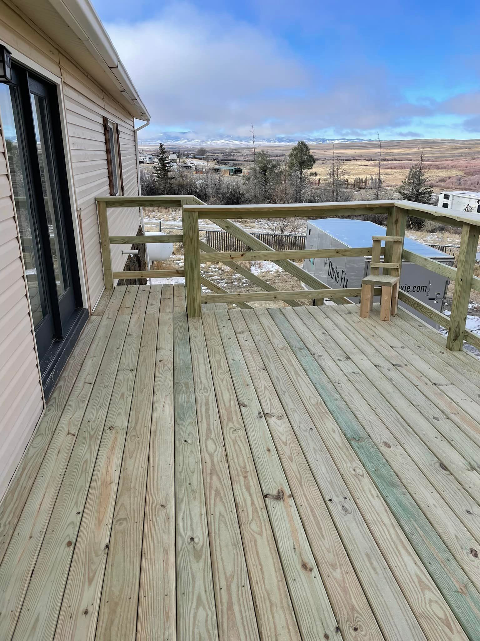 Wooden deck with railing attached to a light-colored house. Snowy landscape visible in the distance.
