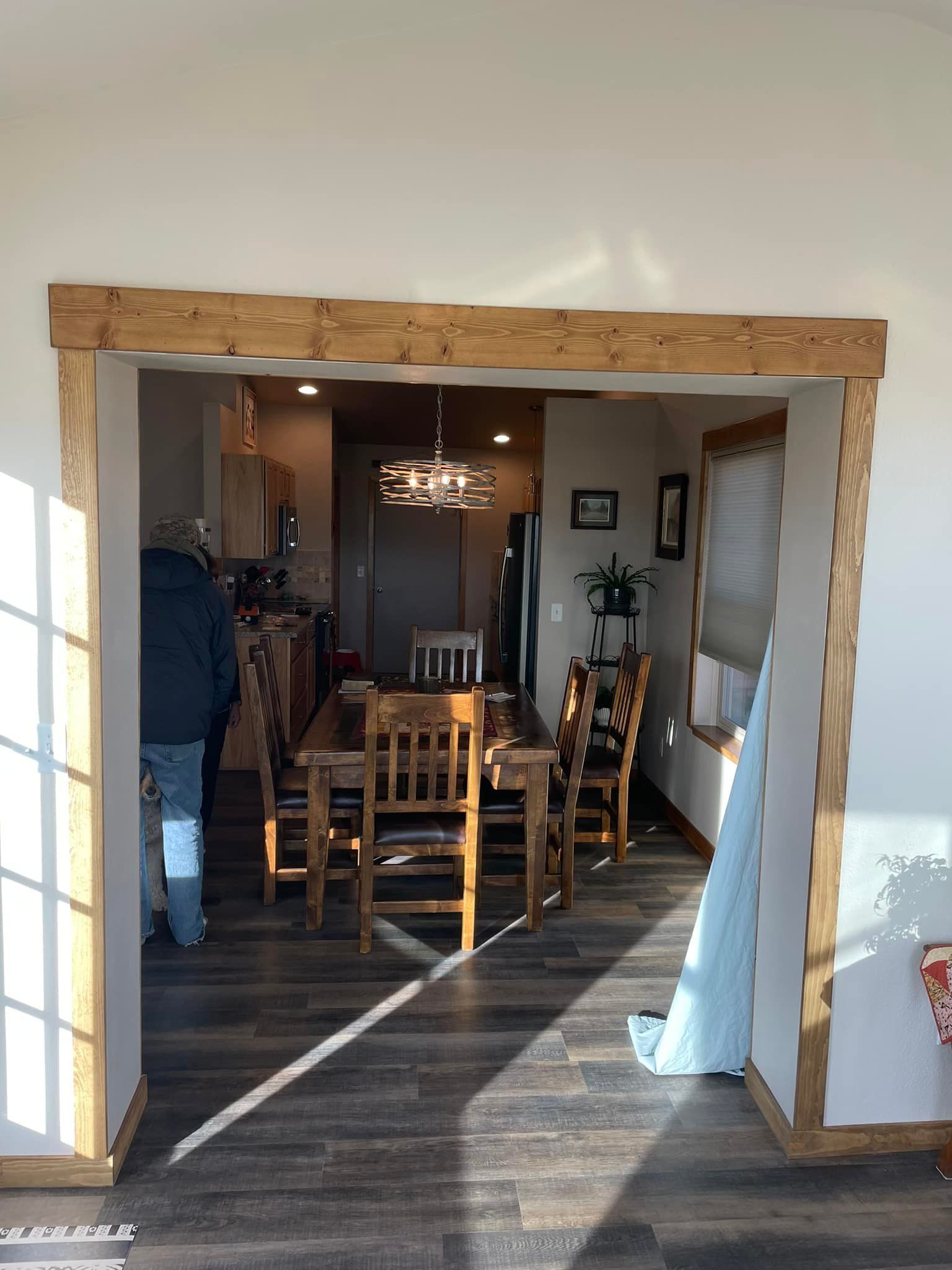 Wooden doorway frame into a dining room with a table, chairs, and chandelier.