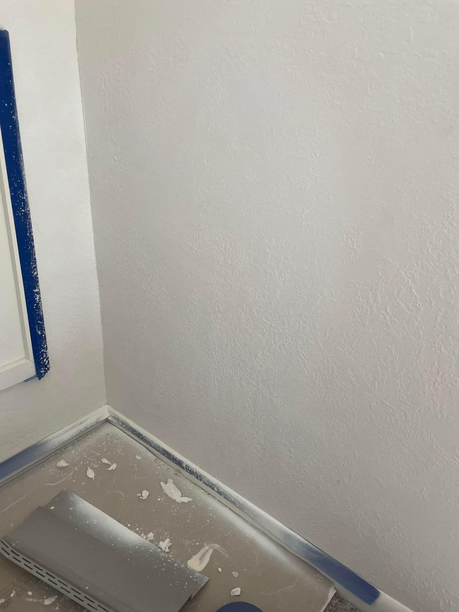 White textured wall with blue painter's tape on window and floor trim.