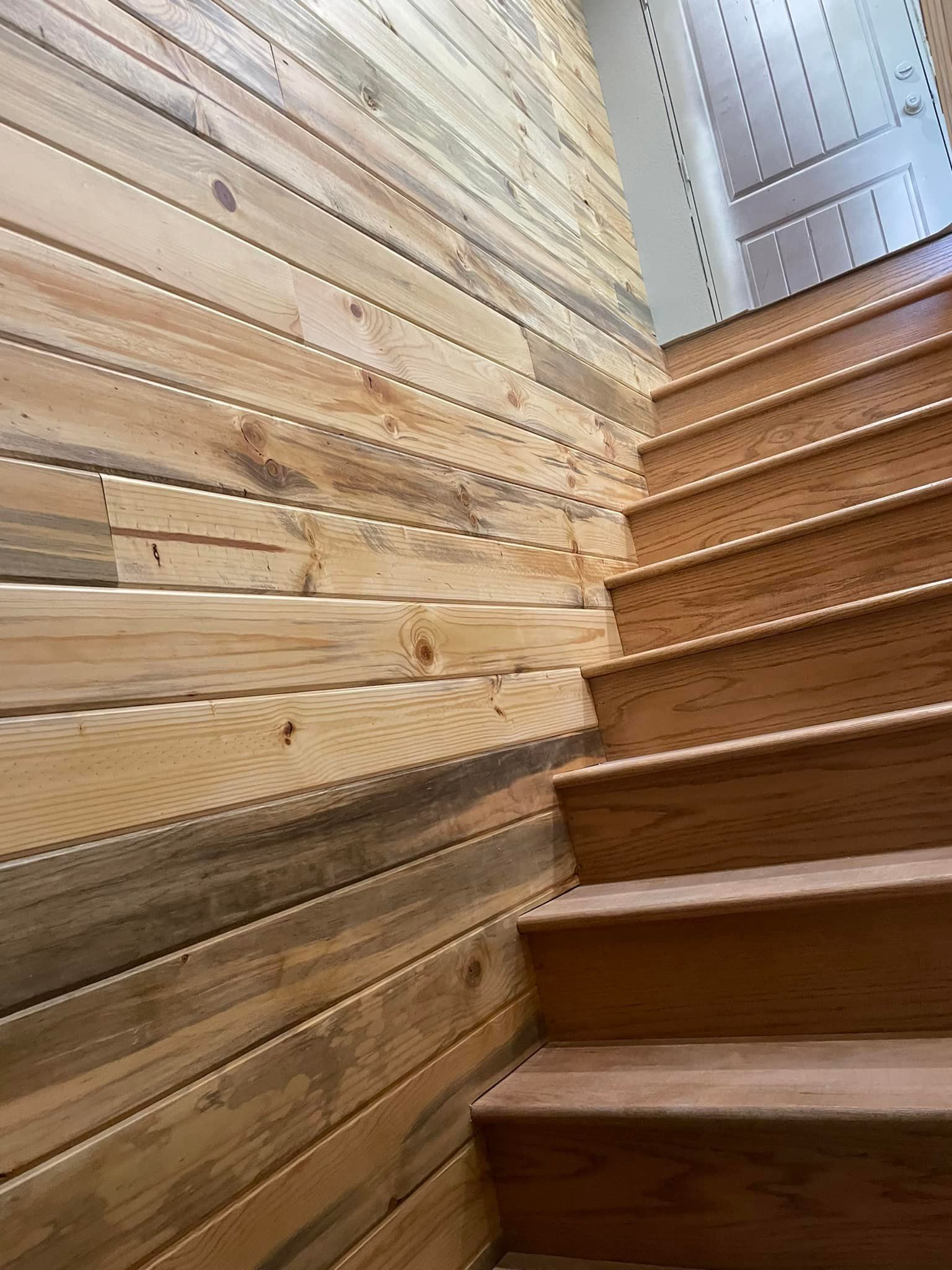 Wooden staircase with wood-paneled wall. The stairs and wall are light brown and are in a corner of a building.