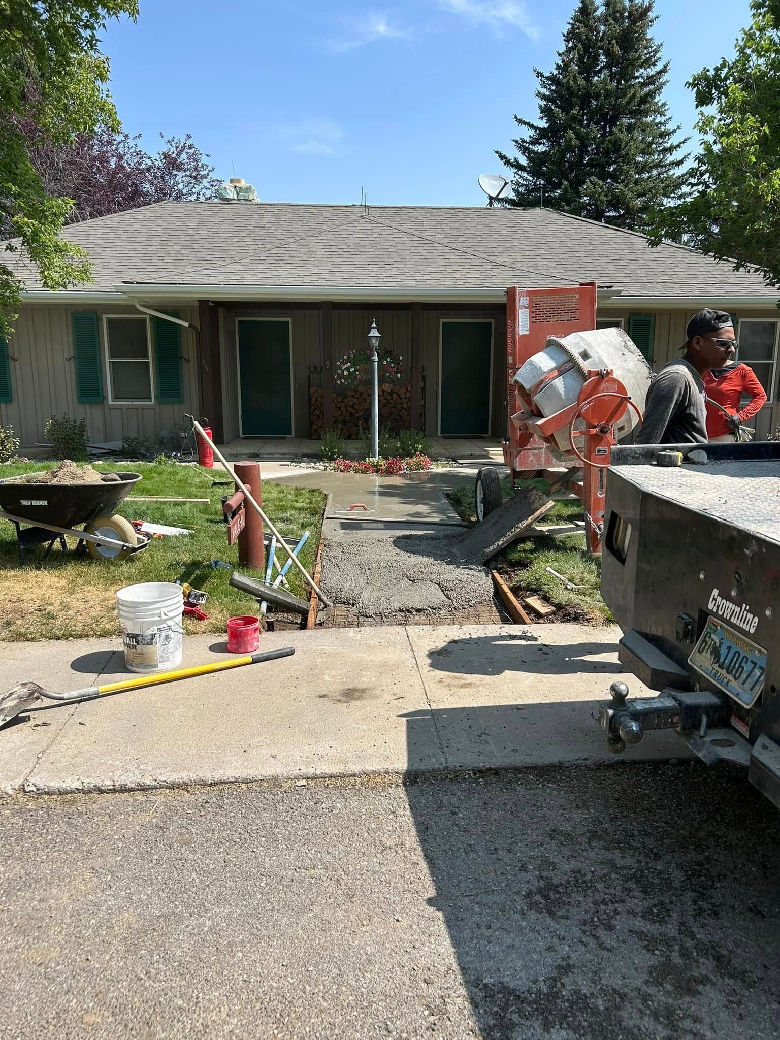 Concrete work in progress at a residential building: a cement mixer, concrete walkway, and a worker near a truck.