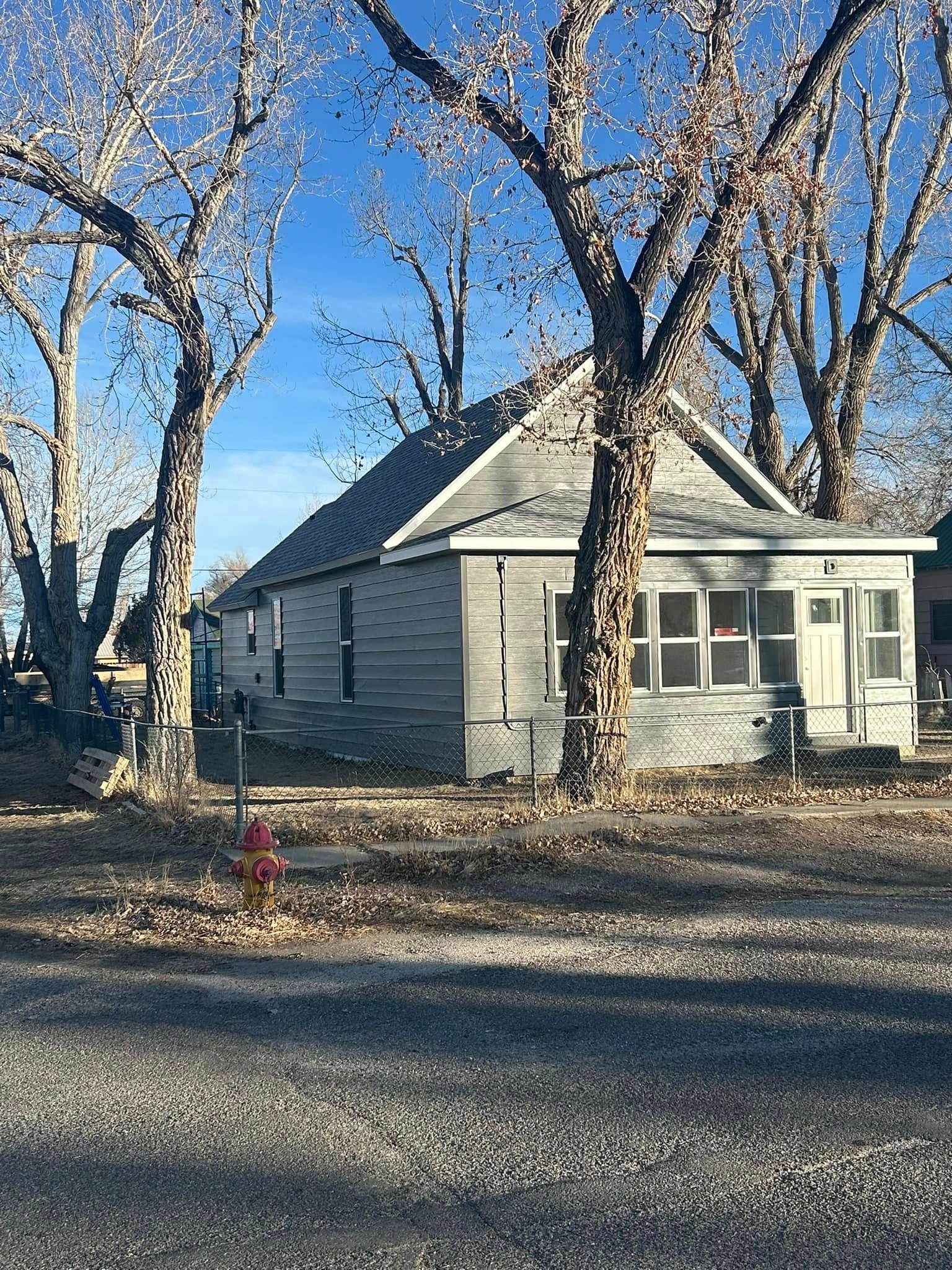 Gray house with trees, fire hydrant, and blue sky.