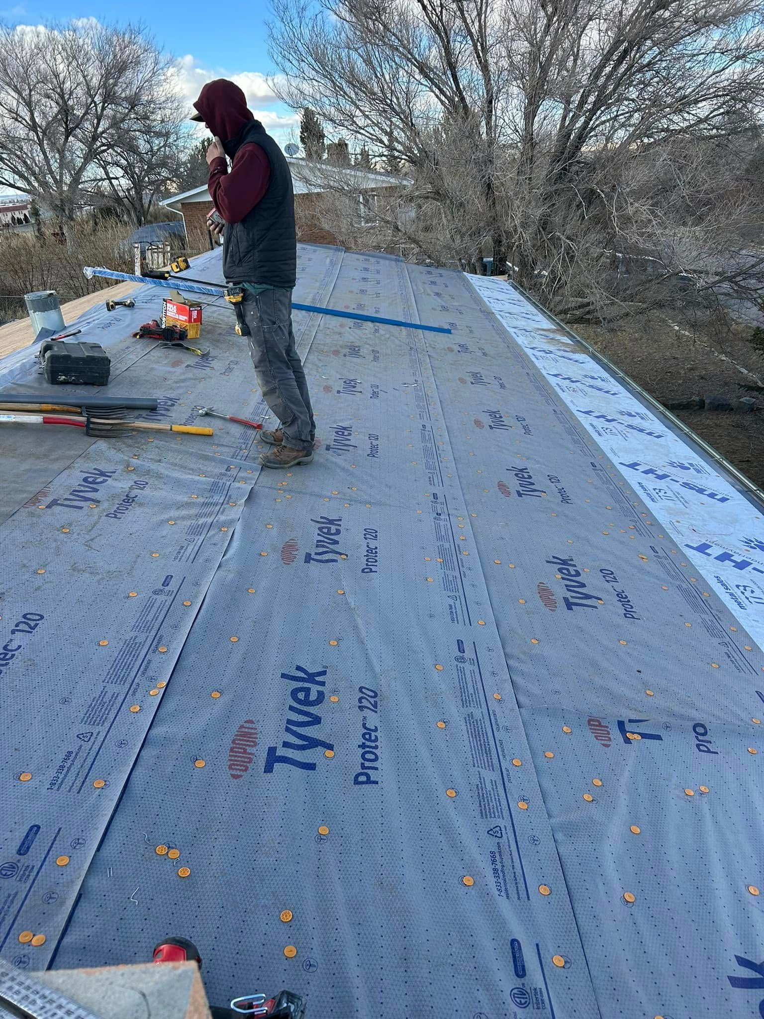 Roofer on a roof, wearing a hoodie, working on a roof with tools and Tyvek underlayment.