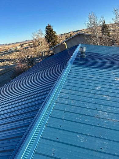 Blue metal roof with a ridge, set against a background of hills and a clear blue sky.