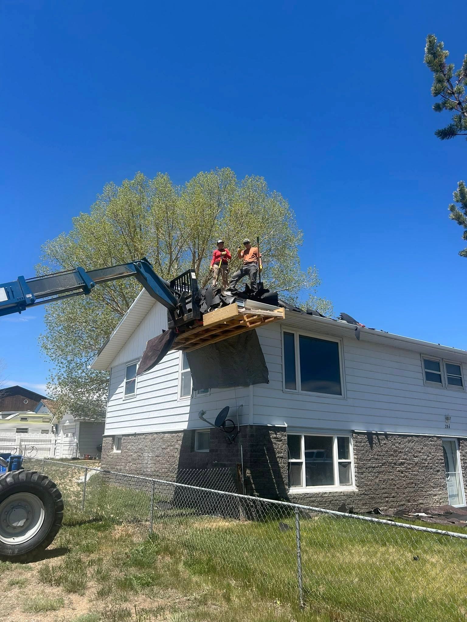 Two workers in a lift basket repairing a house exterior on a sunny day.