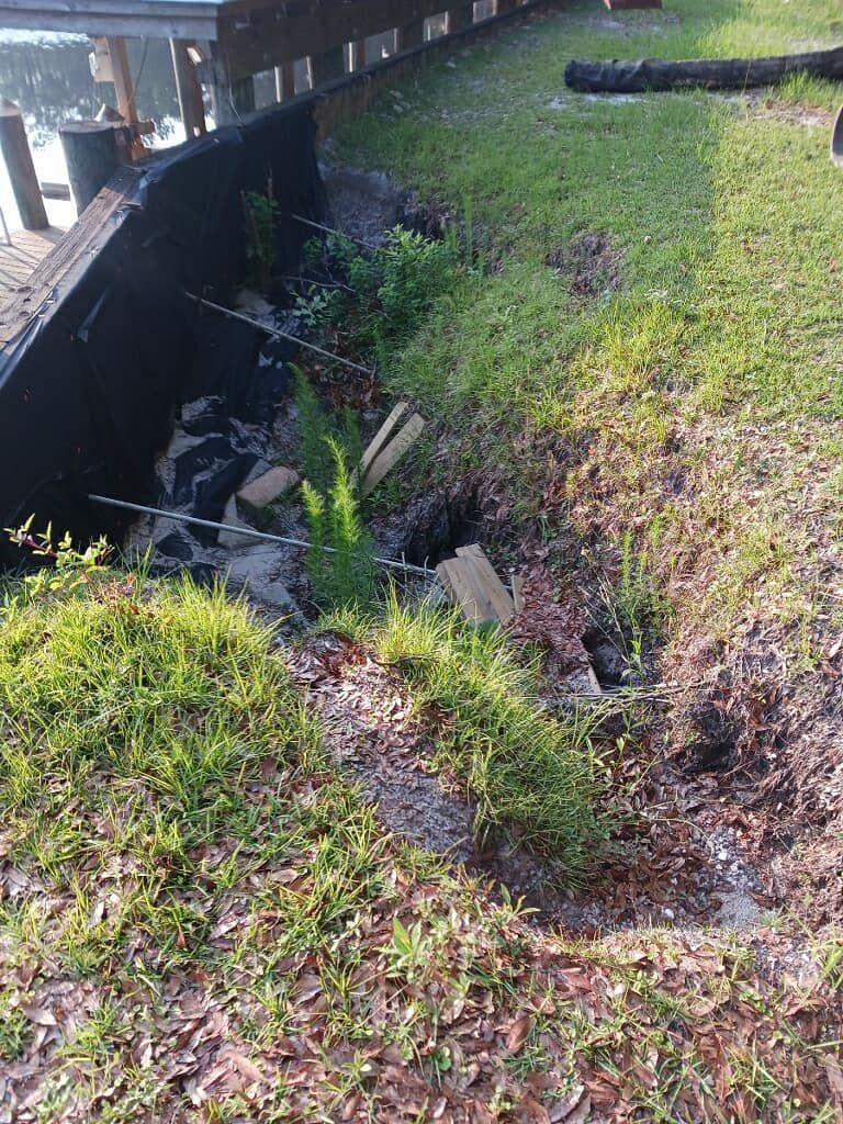 Erosion along a grassy bank next to a dark wall with concrete debris. 