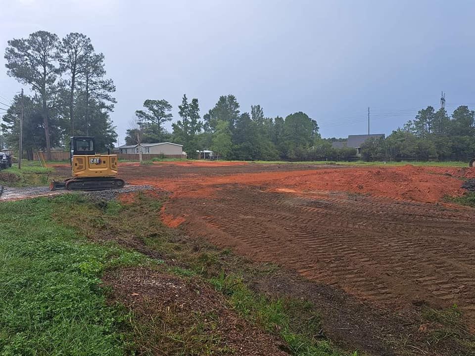 An excavator sits on a cleared construction site with red dirt and green grass. 