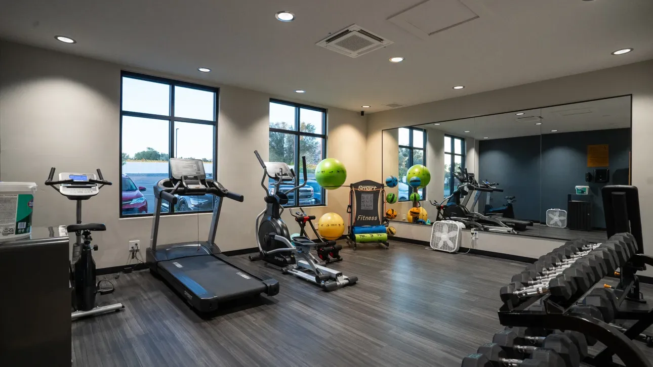 A gym with a treadmill , exercise bike , dumbbells , and a large mirror.