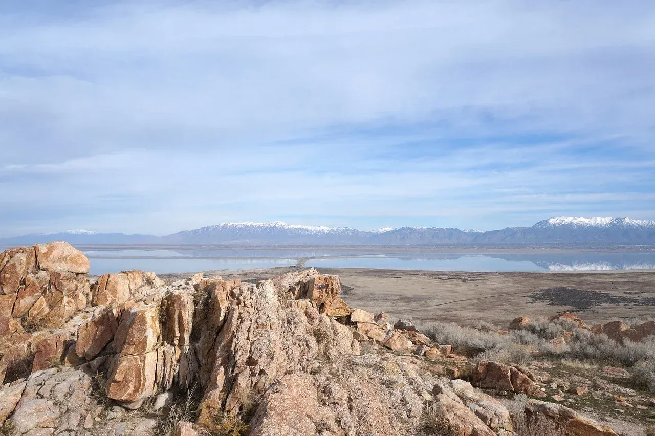 A rocky cliff overlooking a lake with mountains in the background.