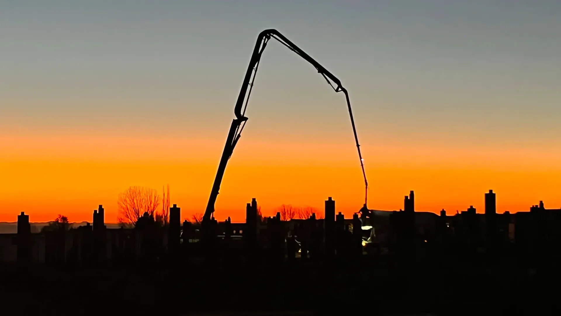 A large crane is silhouetted against a sunset sky