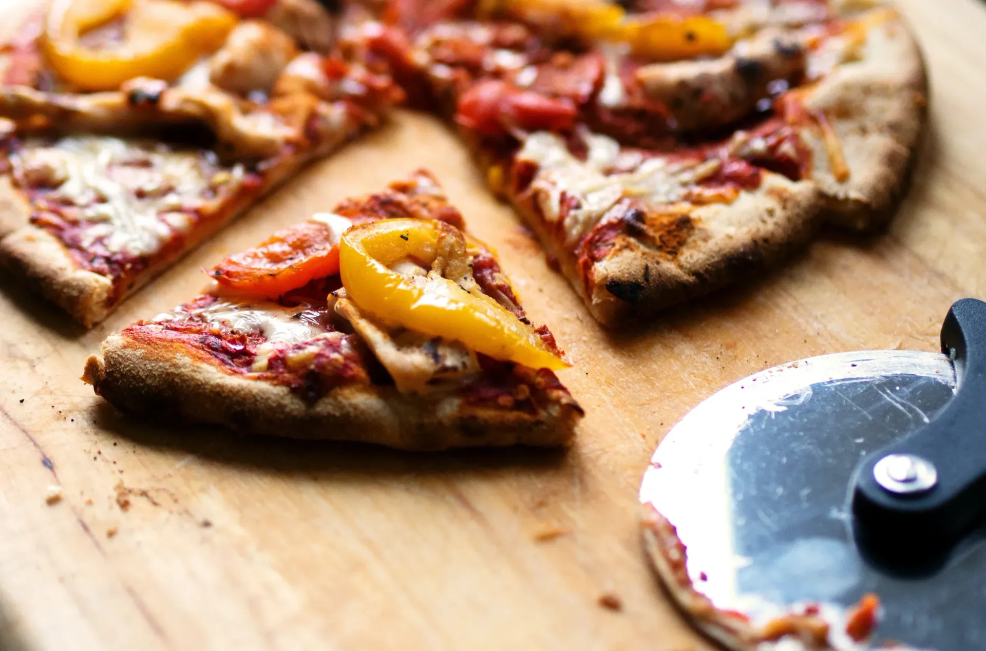 A pizza is sitting on a wooden cutting board next to a pizza cutter.