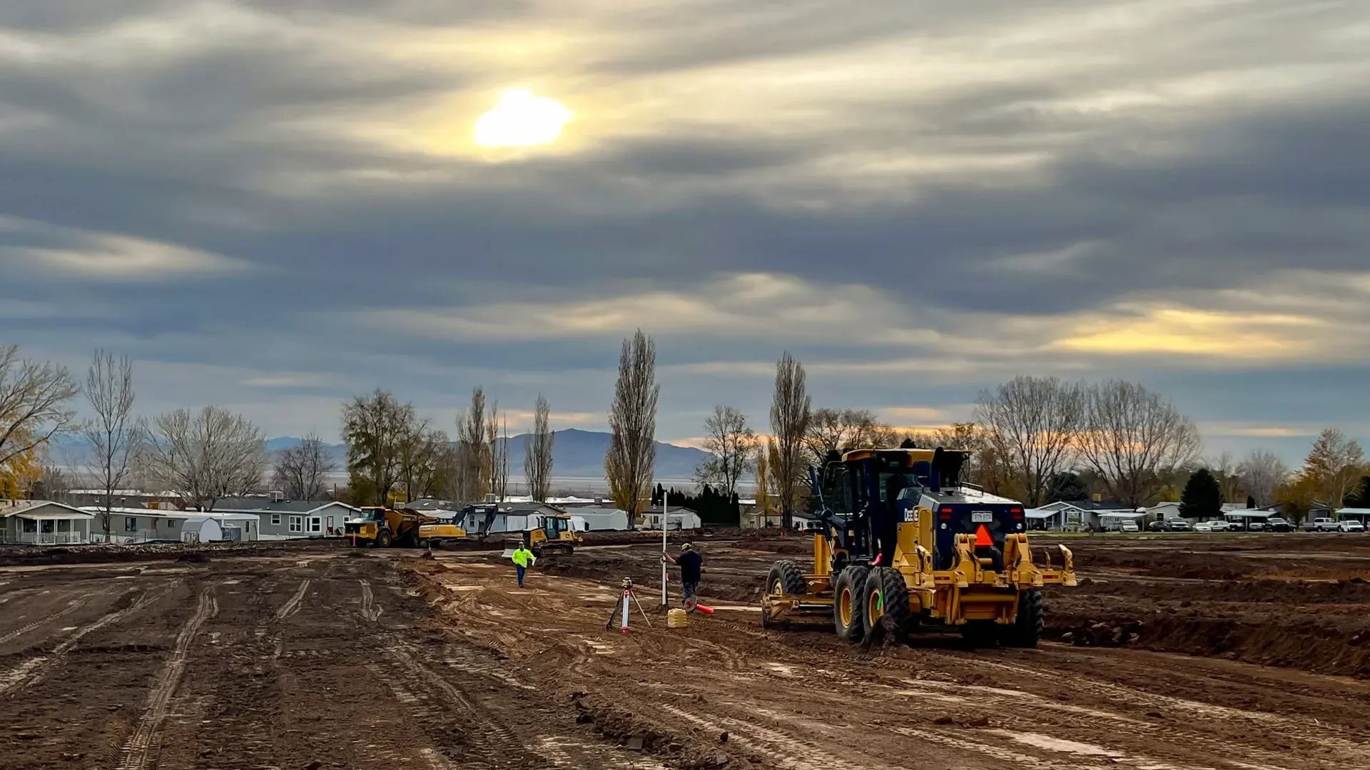 A bulldozer is driving through a muddy field on a cloudy day.