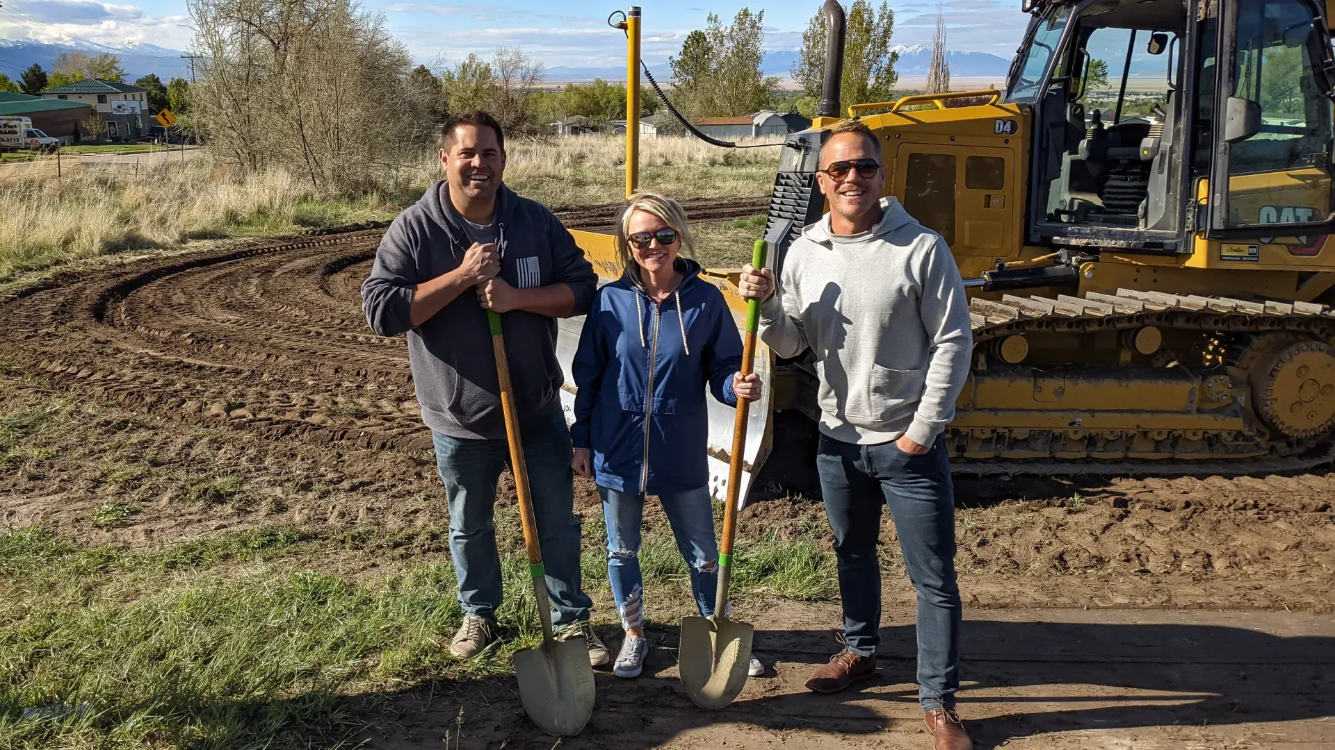 Three people are standing in front of a bulldozer holding shovels.