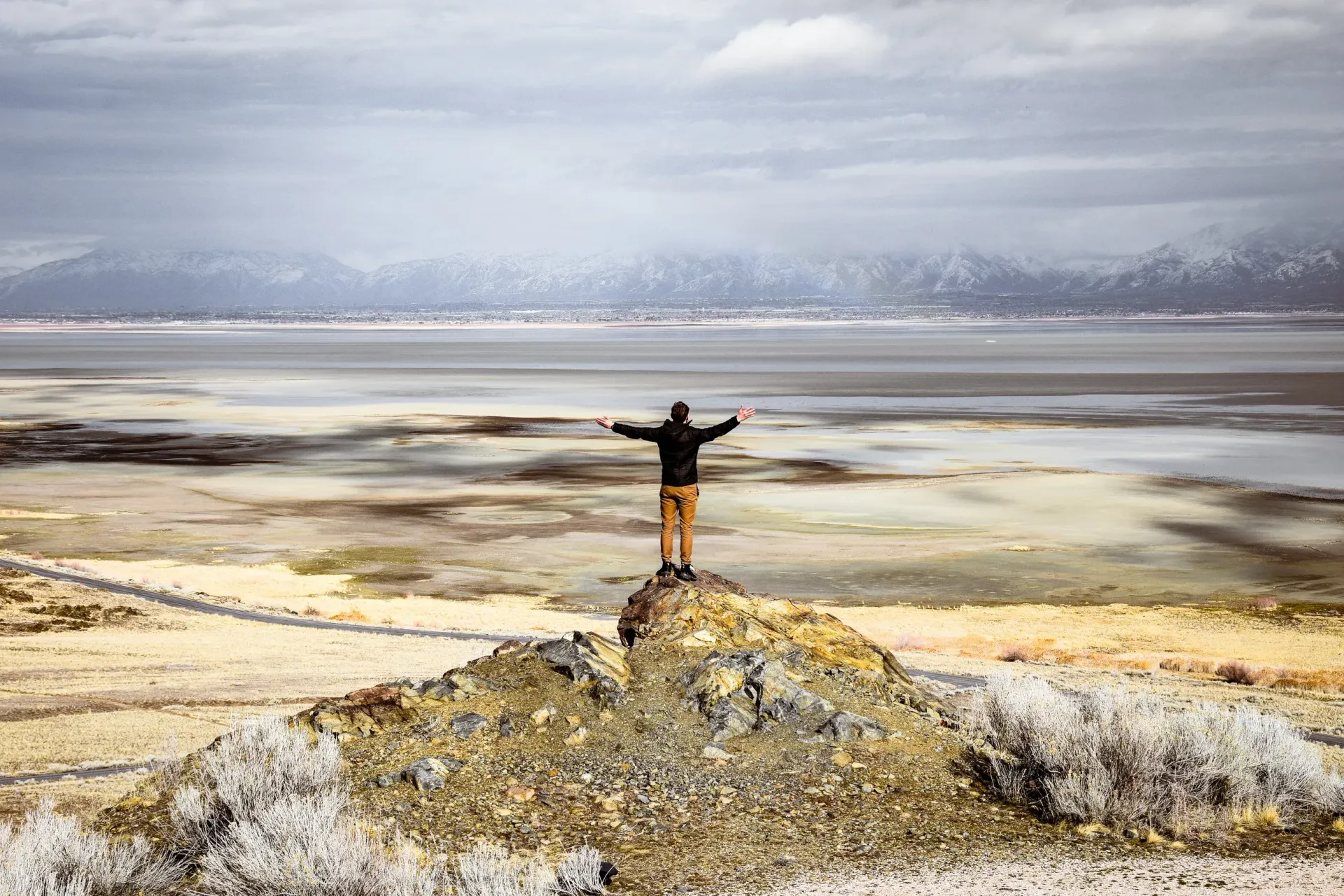 A person is standing on top of a rock overlooking a body of water.