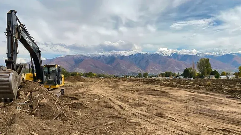 A large excavator is digging a dirt field with mountains in the background.