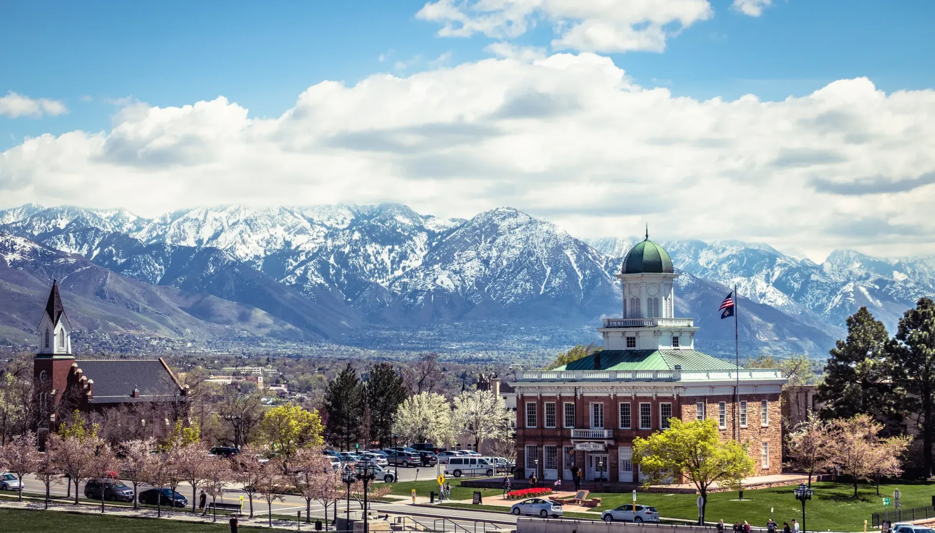 A large building with a green roof is surrounded by trees and mountains in the background.