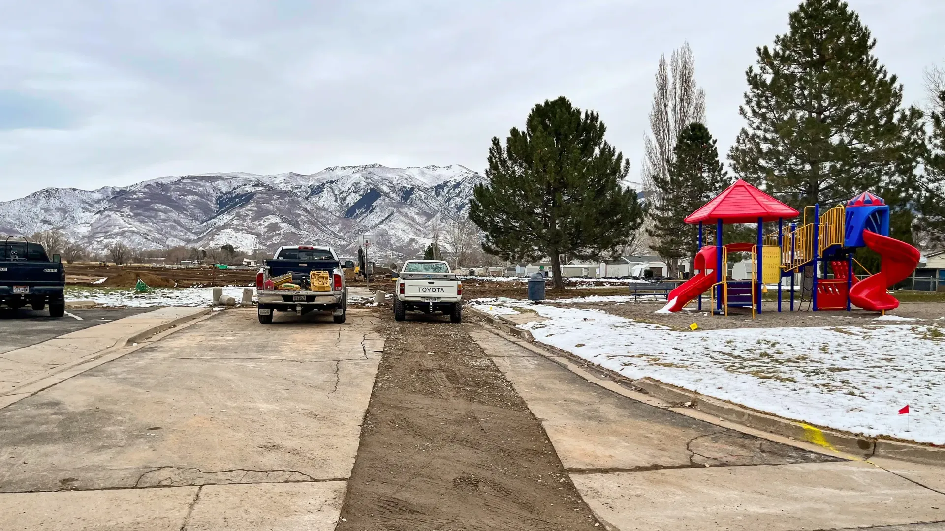 A park with a playground and cars parked on the side of the road.