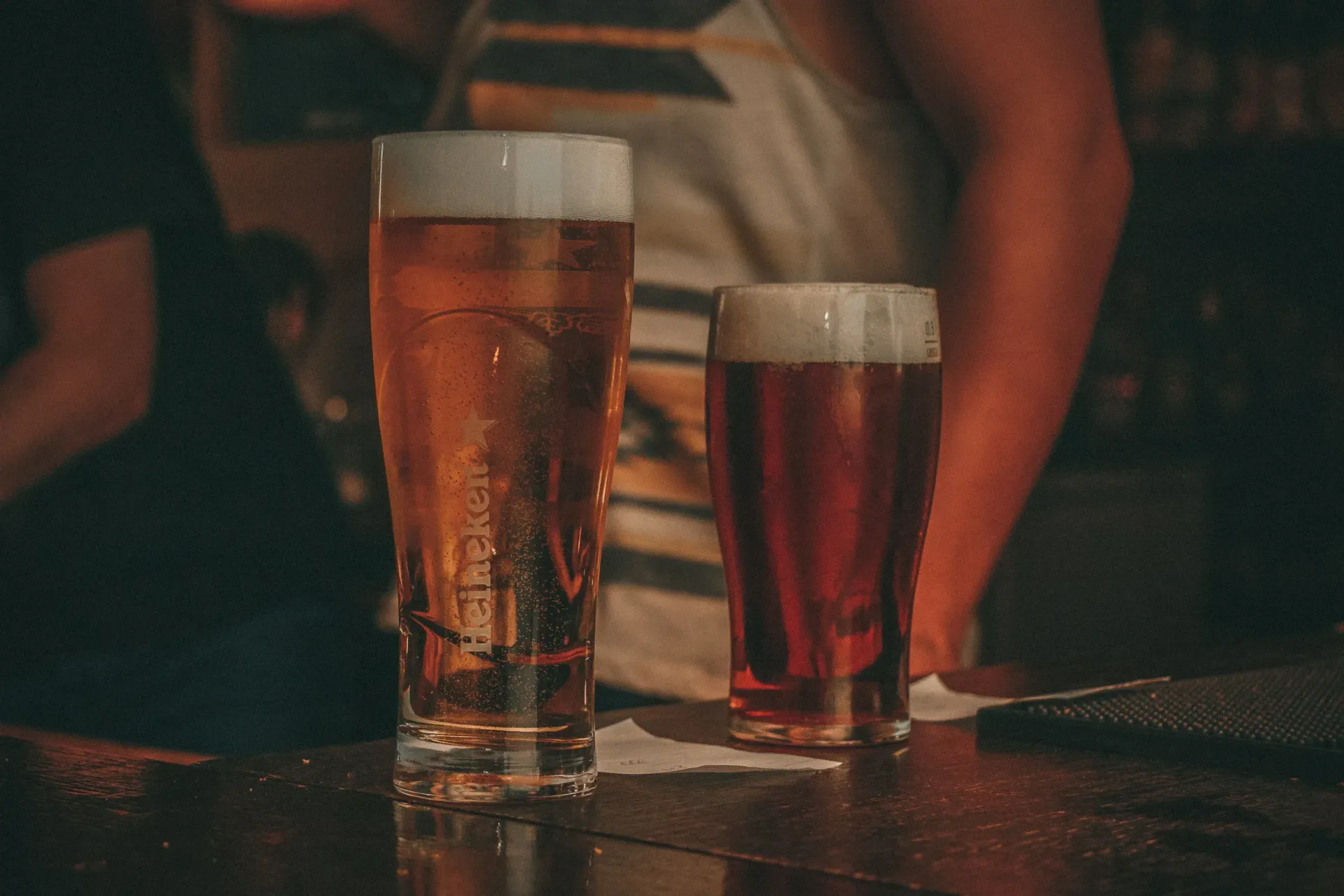 Two glasses of beer are sitting on a bar counter.