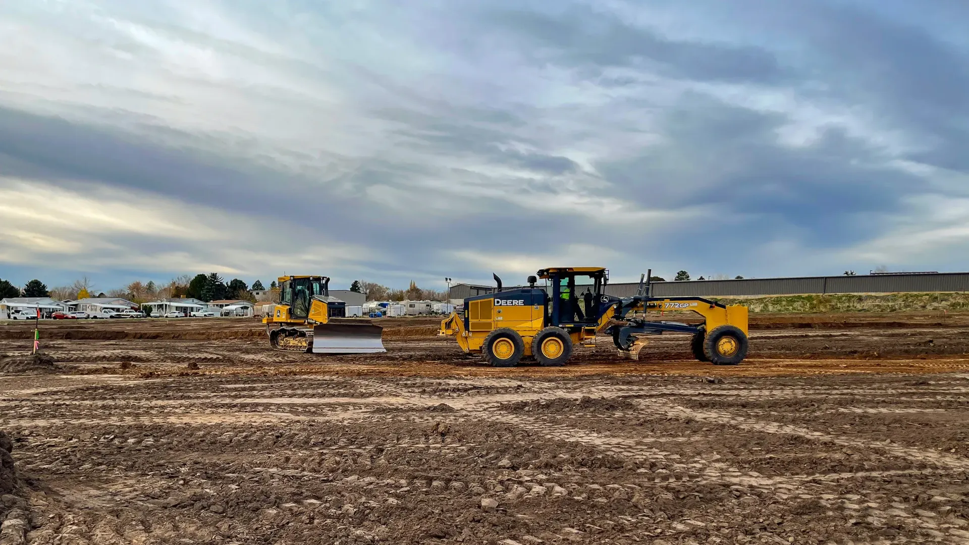 A couple of tractors are driving through a dirt field.