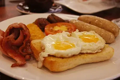 A plate of food with eggs , bacon , tomatoes , sausages and toast on a table.