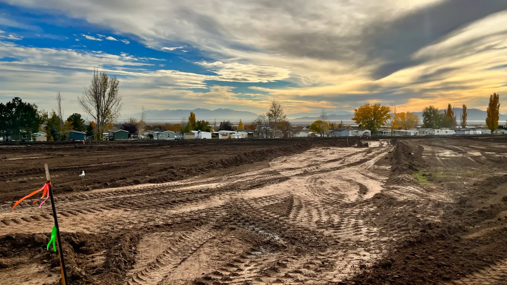 A dirt road going through a muddy field with a sunset in the background.