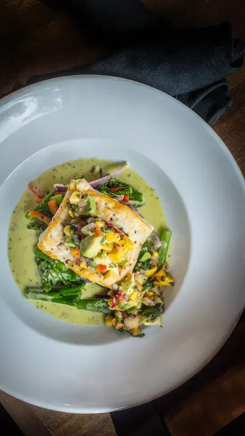 A white plate topped with a piece of fish and vegetables.