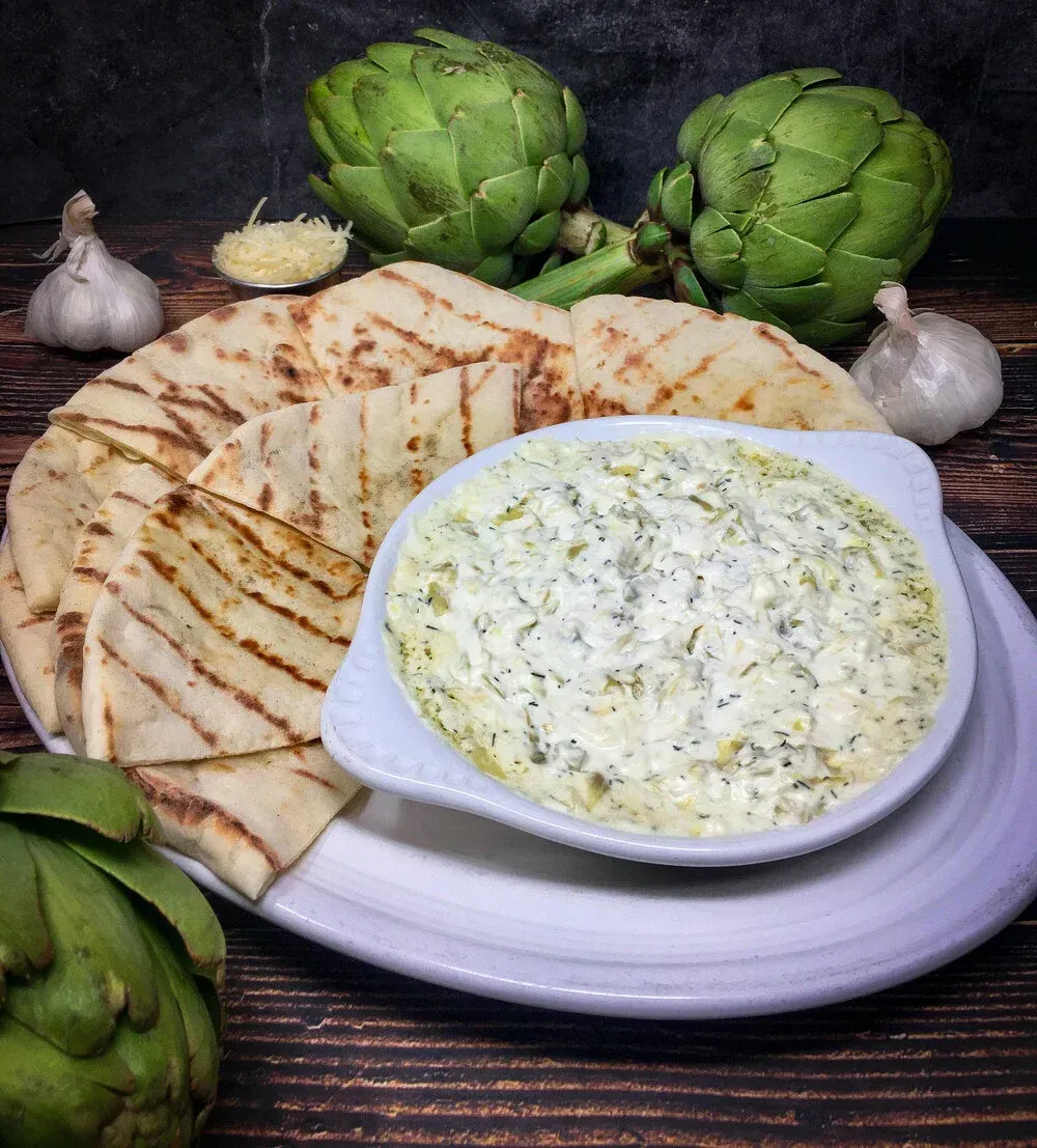 A plate of food with artichokes and pita bread and a bowl of dip