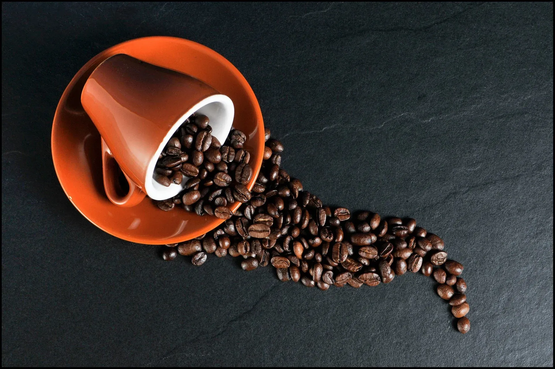 Coffee beans spilling out of an orange cup on a saucer