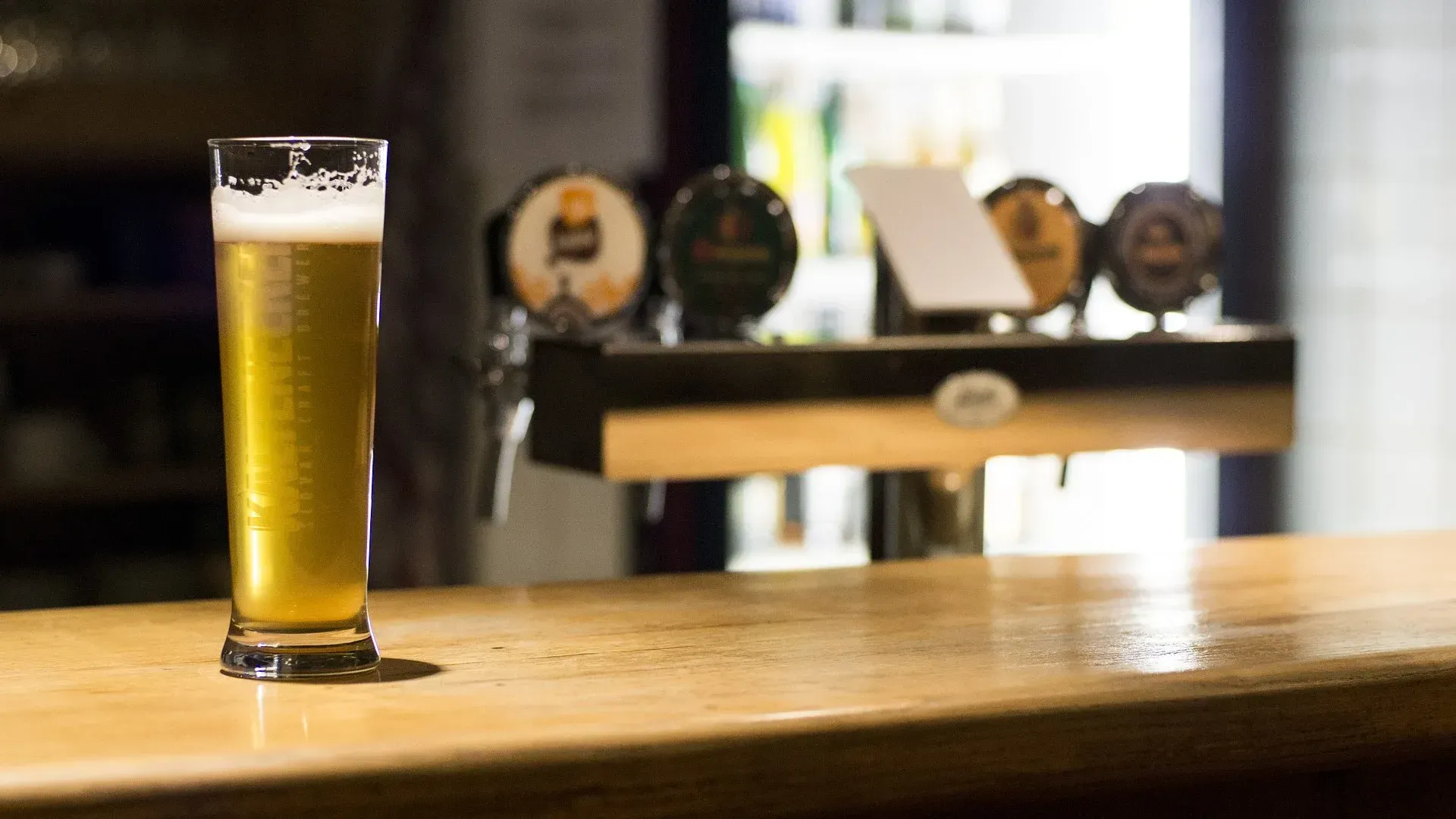 A glass of beer is sitting on a wooden bar.