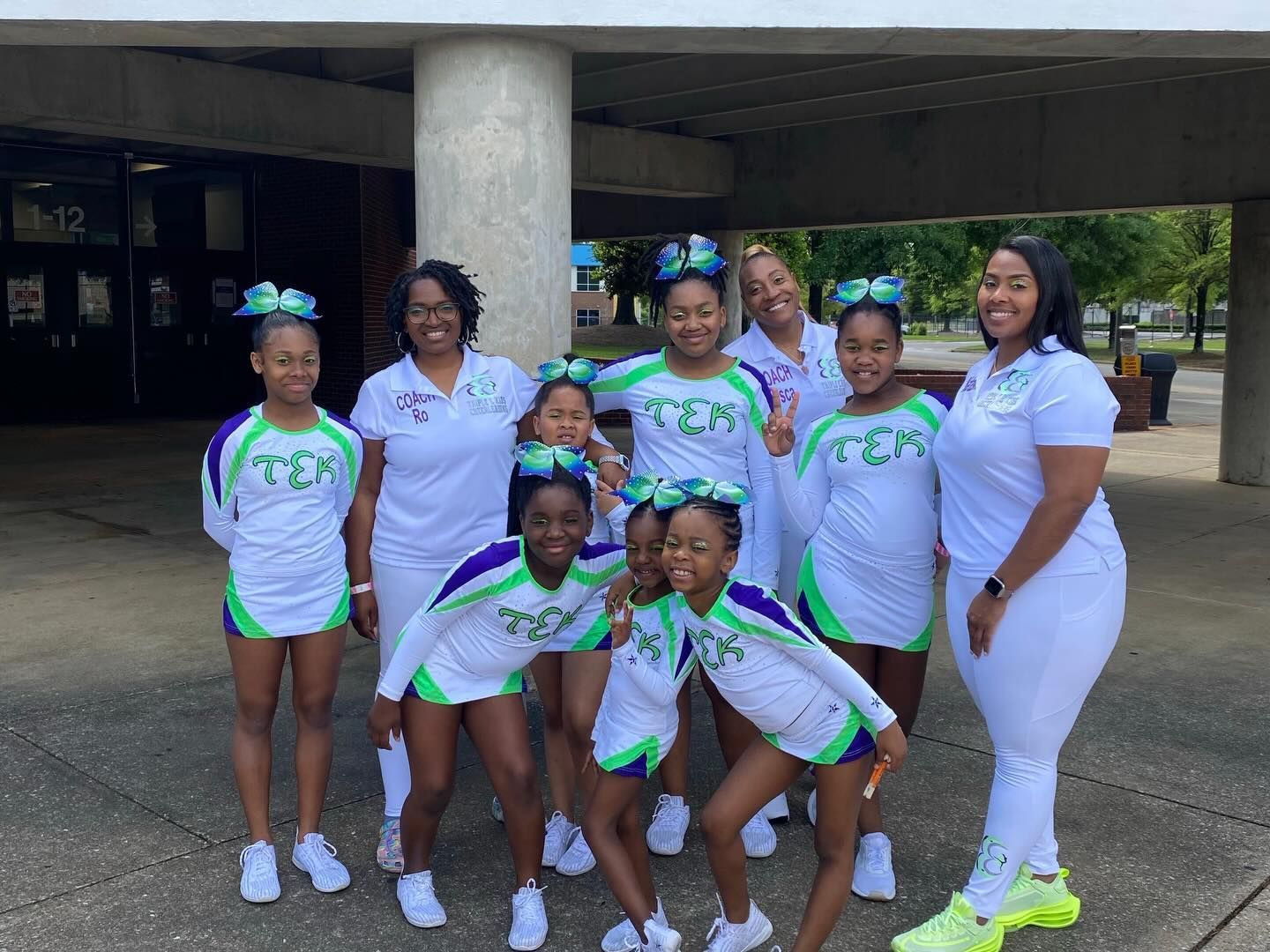 Seven people in white-and-green uniforms posing outdoors under a concrete overhang.