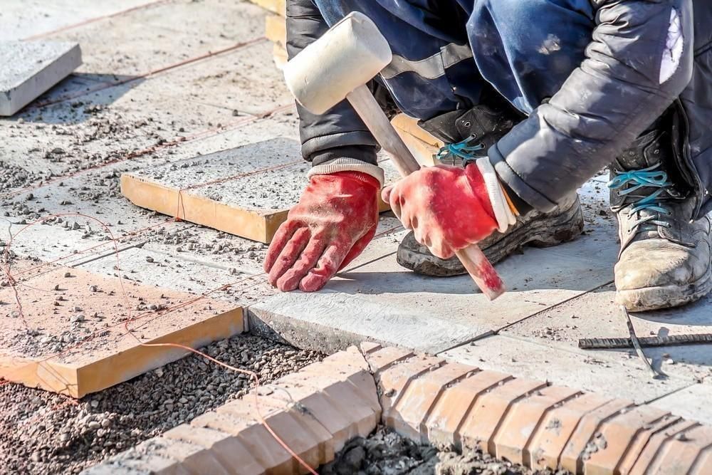 a man is working on a sidewalk with a hammer .