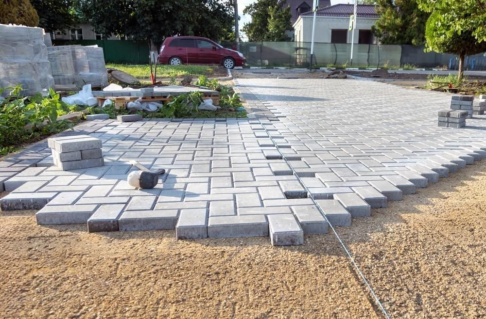 a driveway is being built with bricks and a car is parked in the background .