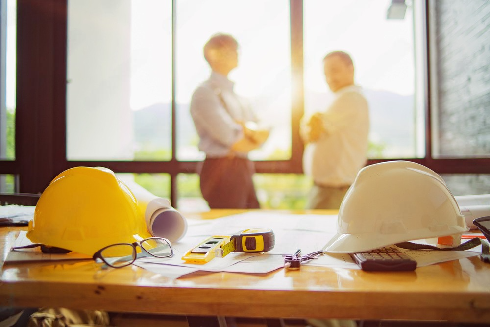 a table with hard hats , glasses , a tape measure , and a blueprint on it .