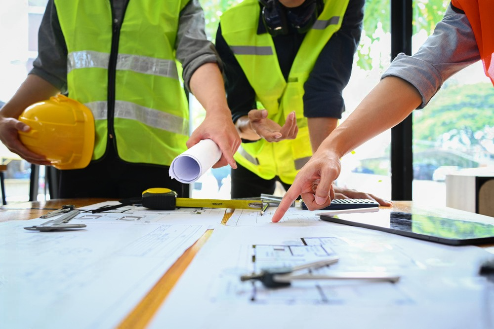 a group of construction workers are looking at a blueprint on a table .