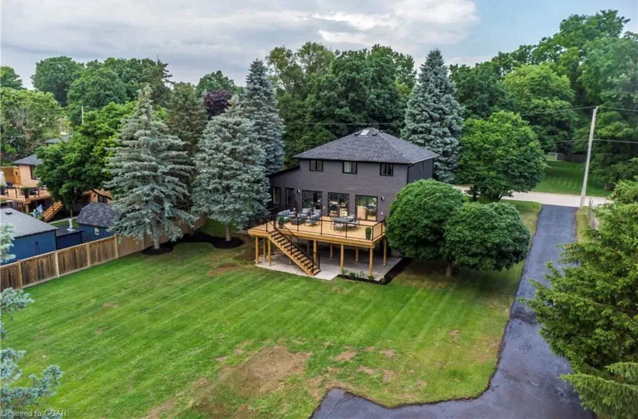 Dark house with a wooden deck, surrounded by trees and a green lawn.